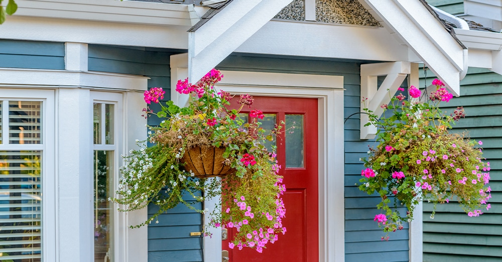 An exterior view of a home with a red door and colorful hanging flower baskets symbolizes the concept of estate planning and protecting family assets.