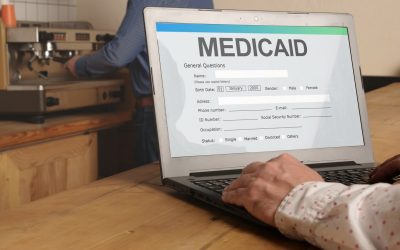 A Pair Of Hands On A Laptop With A Screen That Says “Medicaid” With An Application Form Below It.
