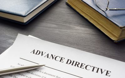 A Piece Of Paper On A Desk With “advanced Directive” Written At The Top, Bordered By Books, A Pair Of Glasses, And A Pen.