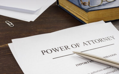 A Piece Of Paper On A Desk With “power Of Attorney” Written At The Top, Bordered By A Book, A Pair Of Glasses, And A Pen.