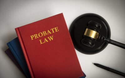 Top View Of A Red Probate Law Book On Top Of Two Blue Books With A Black Gavel And A Pen On A White Desktop.
