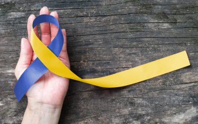 A Hand Holding A Blue And Yellow Ribbon With The Down Syndrome Awareness Month Colors On A Wooden Table.