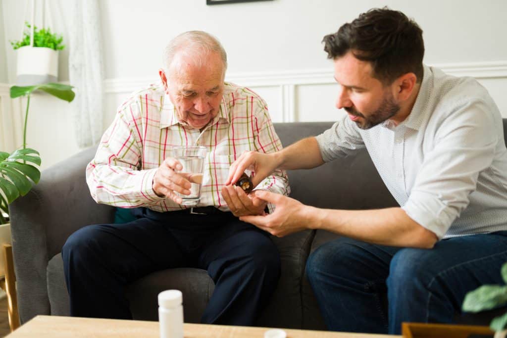 A man gives his father daily medications as his family caregiver. 