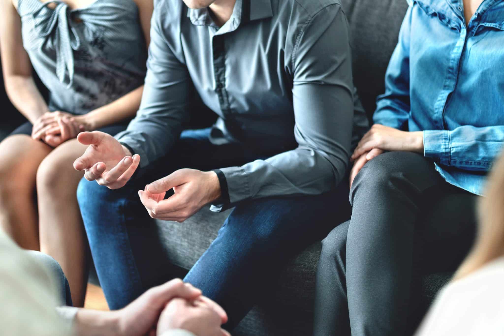 A partial view of people sitting in a group on sofas, representing a family managing a dispute or discussing estate planning.