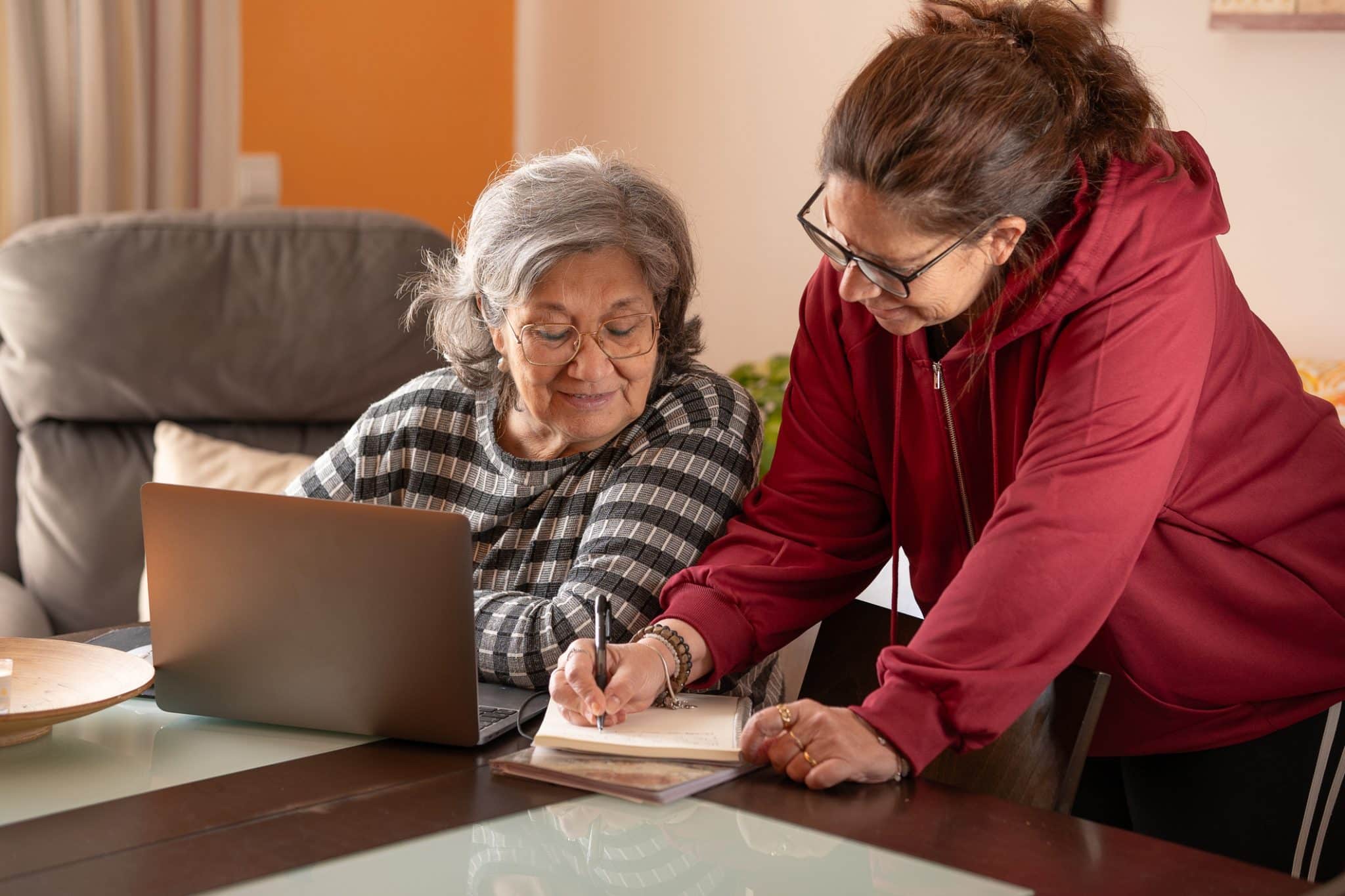 An older woman and her adult daughter sit together at a kitchen table reviewing documents related to Medicaid planning.