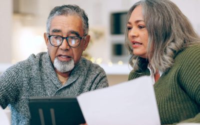 An older man and his adult daughter sit at a kitchen table reviewing estate planning documents together.