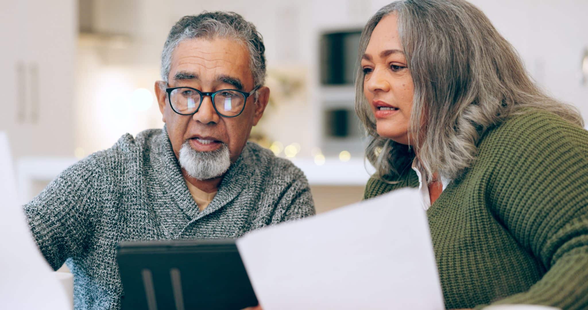 An older man and his adult daughter sit at a kitchen table reviewing estate planning documents together.