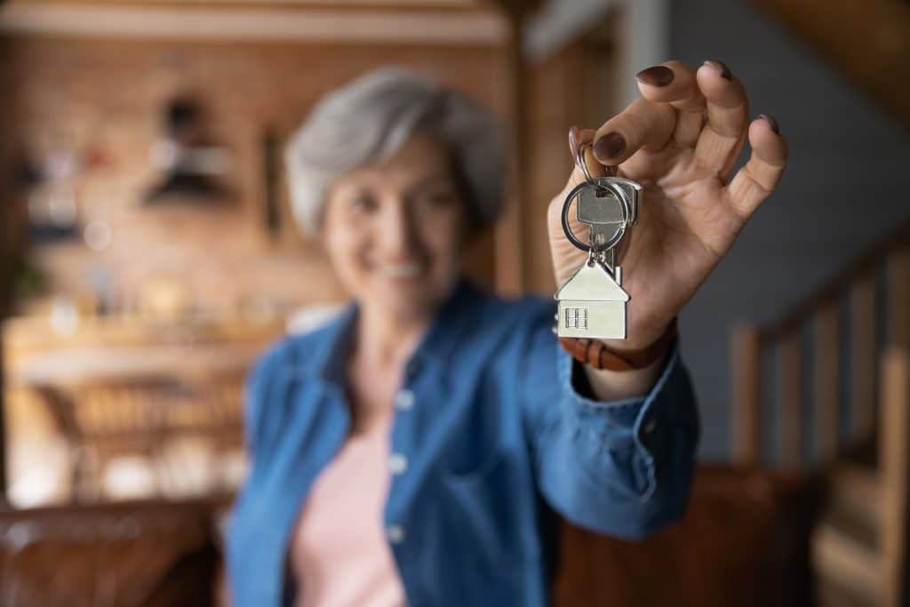 A senior woman holds up keys representing a rental property she owns.