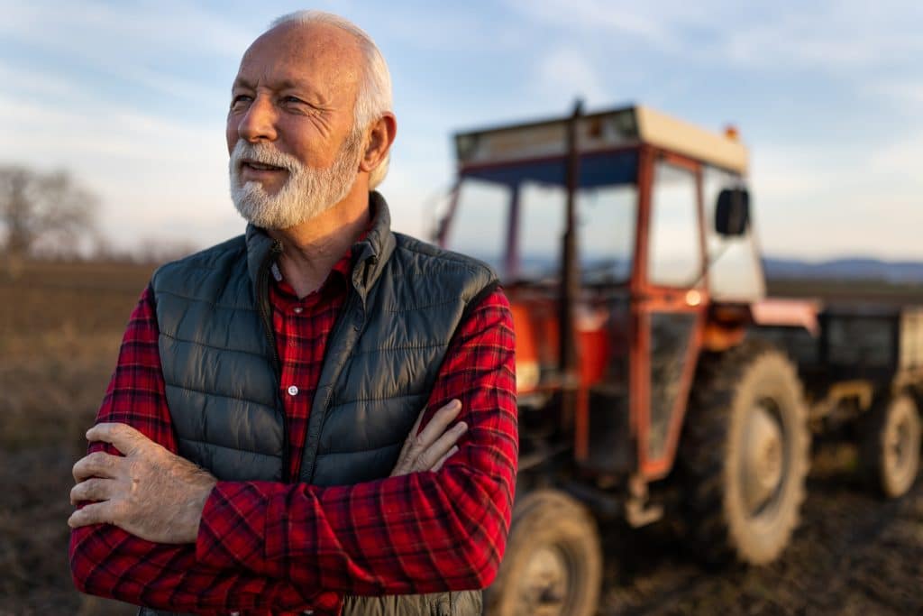An elder farmland owner looks out at his field at sunset.